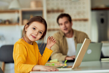 Obraz premium A cute little girl sitting on the table with a toy laptop, smiling at the camera.