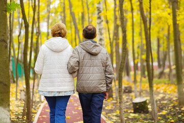 Fototapeta premium Elderly women and man walk in park at autumn day, back view