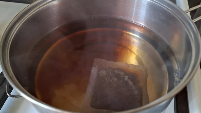 Brewing a tea bag in a stainless pot, steaming  water, time lapse