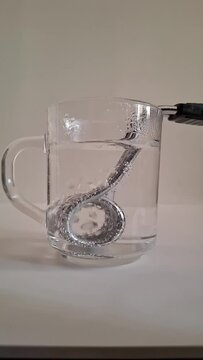Boiling water in glass tea cup with immersion heater, bubbles closeup