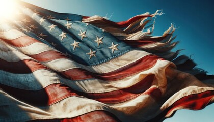 Close-up of a frayed American flag against a blue sky, symbolizing resilience and patriotism - obrazy, fototapety, plakaty