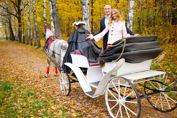 Obraz premium Happy couple are in coach with horse and coachman in autumn park
