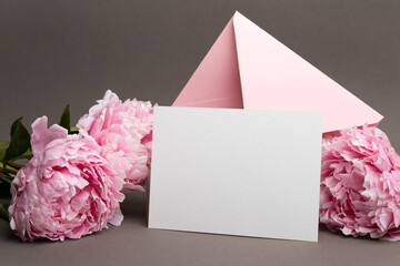Blank wedding invitation card mockup with pink envelope and fresh peony flowers, copy space