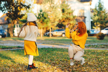 Mother and child girl throwing leaves in autumn park. Happy family enjoying autumn day.