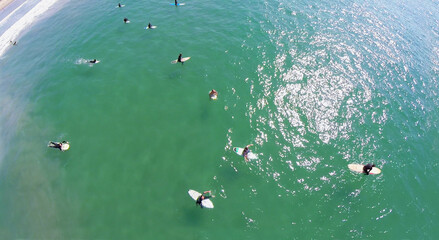  Group of surfers wait for wave in water at autumn sunny day. Aerial view. Surfing professional contests started in 1975.