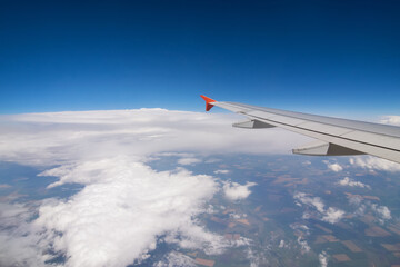 Naklejka na ściany i meble Wing of flying airplane, land, clouds in blue sky, view from window