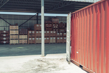 Warehouse area filled with a red container with open doors and wooden crates opposite which processed marble products are placed under a metal roof