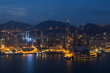 Skyscrapers with illumination, shore front and mountains in Hong Kong, China at dark night, view from New World Center