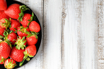 Organic strawberries in a black plate on a light wooden background, top view, copy space