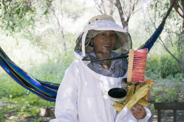 Young, Latin, brunette woman, dressed in a beekeeping suit, holding elements to work in her hands.
