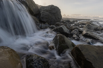 A waterfall is flowing over a rocky shore