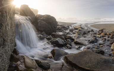 A stream of water flows between large rocks on a beach