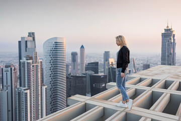 Woman stands on roof of skyscraper in Dubai, BayGate and Executive Towers at evening