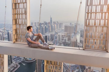 Poster Helix-Brücke Roofer sits on concrete cross beam of Cayan Tower (Infinity Tower) in Dubai, UAE