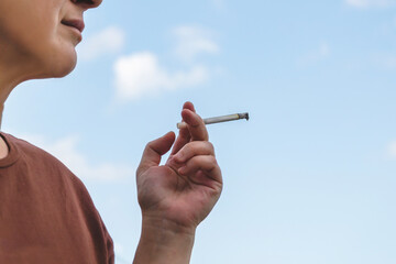 woman holding lit cigarette in her hand against the blue sky - obrazy, fototapety, plakaty