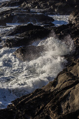 The ocean waves are crashing against the rocks, creating a powerful