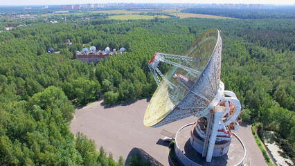 Antenna  of radio telescope RT-64 Bear Lakes among forest and cityscape on horizon at summer sunny...