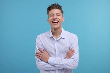 Young man with crossed arms laughing on light blue background
