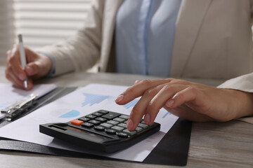 Woman using calculator at light wooden table in office, closeup