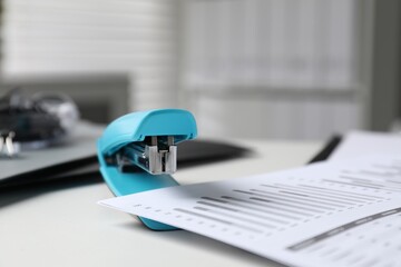 Stapler with document on white table indoors, closeup