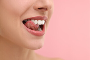 Woman with beautiful lips licking her teeth on pink background, closeup. Space for text