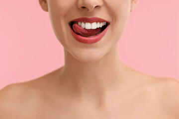 Woman with beautiful lips licking her teeth on pink background, closeup