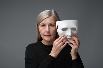 Multiple personality concept. Woman with mask on gray background