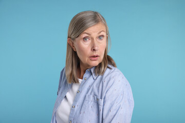 Portrait of surprised senior woman on light blue background
