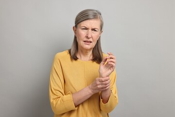 Arthritis symptoms. Woman suffering from pain in wrist on gray background