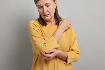 Arthritis symptoms. Woman suffering from pain in elbow on gray background