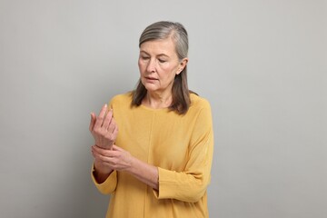 Obraz premium Arthritis symptoms. Woman suffering from pain in wrist on gray background