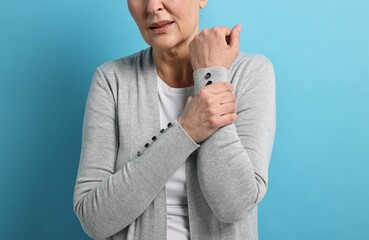Arthritis symptoms. Woman suffering from pain in arm on light blue background, closeup