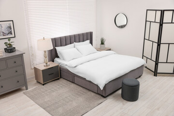 Stylish bedroom interior with large bed, chest of drawers and lamp