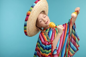 Cute girl in Mexican sombrero hat and poncho singing with maracas on light blue background