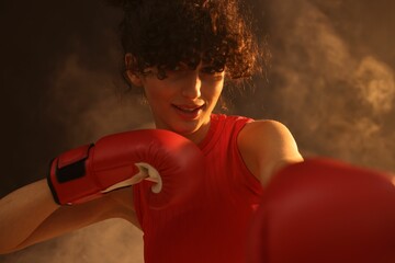 Beautiful young woman with boxing gloves on color background in neon lights and smoke
