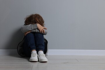 Child abuse. Upset boy sitting on floor near grey wall, space for text