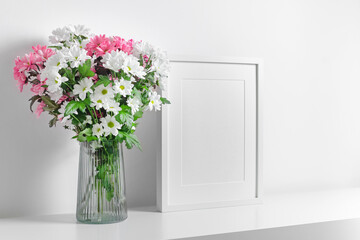 Blank portrait frame mockup in white interior with fresh flowers bouquet