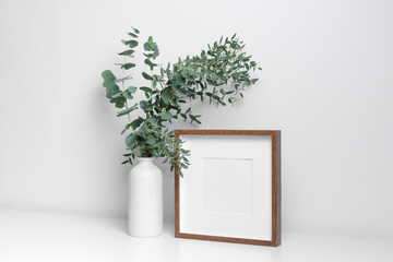Square wooden frame mockup in white interior with fresh eucalyptus plant