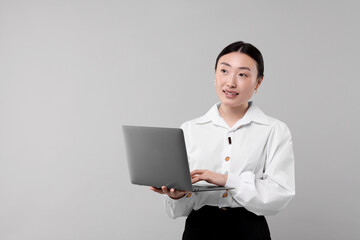 Portrait of smiling businesswoman with laptop on grey background. Space for text
