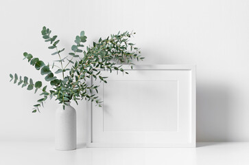 Blank horizontal frame mockup in white room interior with fresh eucalyptus plant in vase