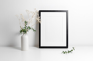 Blank portrait artwork frame mockup in white minimalistic interior with flowers decorations, copy...