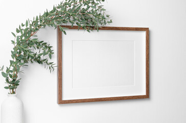 Landscape frame on white wall with natural eucalyptus. Blank mockup for artwork, print or photo presentation.