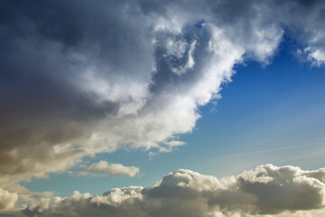 Naklejka na ściany i meble Large cumulonimbus rain clouds cover the blue sky, a cloud in warm sunlight on the blue sky
