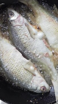 whole vobla fish frying in a cast iron skillet with oil at domestic kitchen.
