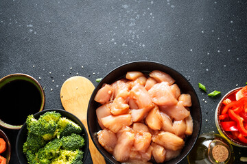 Chicken stir fry with soy sauce and vegetables at black background. Ingredients for cooking, recipe. Flat lay with copy space.