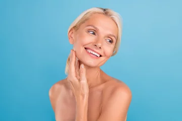 Tuinposter Photo of dreamy cute elderly lady naked shoulders enjoying soft skin arms touch cheekbones isolated blue color background © deagreez