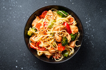 Stir fry chicken with vegetables and noodles at black background. Asian cuisine. Top view with space for design.