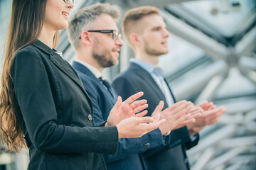 A group of young businessmen applauds at a business conference against the background of a modern office building