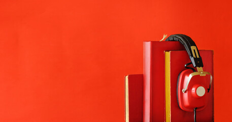 audiobooks concept with row of red books and vintage headphones.Bright red background with large copy space