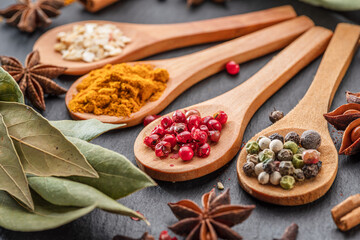 Various types of spices on wooden spoons on a gray stone table. - 755783161